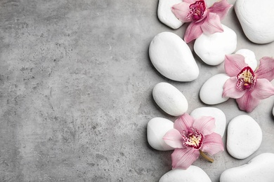 Photo of Zen stones and exotic flowers on grey background, top view with space for text