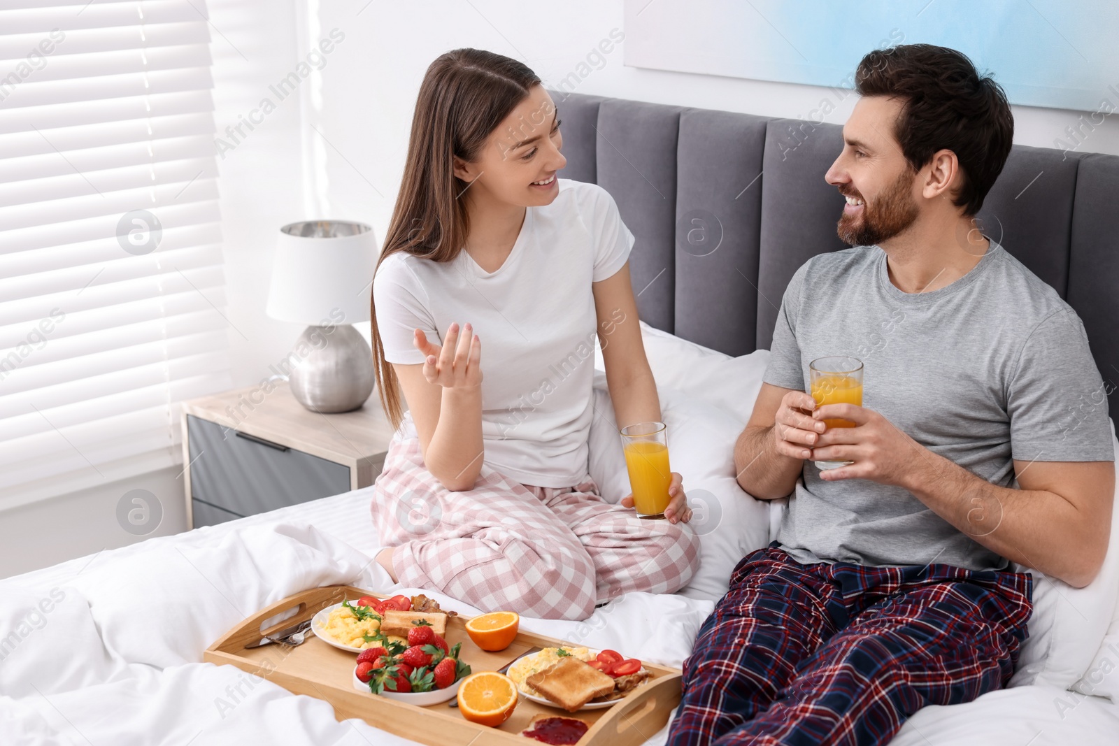 Photo of Happy couple eating tasty breakfast on bed at home