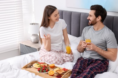 Happy couple eating tasty breakfast on bed at home