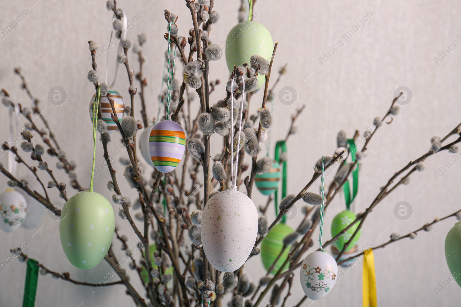 Photo of Beautiful willow branches with painted eggs on light grey background, closeup. Easter decor