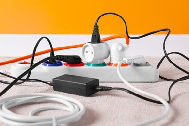 Photo of Power strip with different electrical plugs on white carpet indoors, closeup