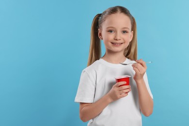Cute little girl with tasty yogurt on light blue background, space for text