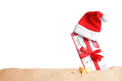 Photo of Airline ticket with red bow and Santa hat in sand near starfish, space for text. Christmas vacation