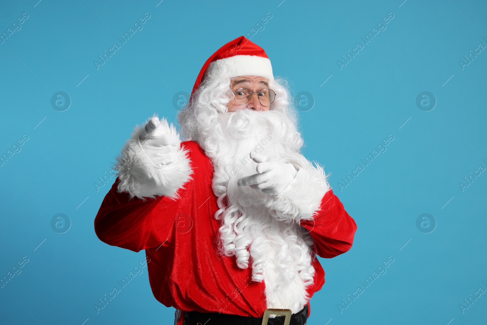 Photo of Merry Christmas. Santa Claus pointing at something on light blue background