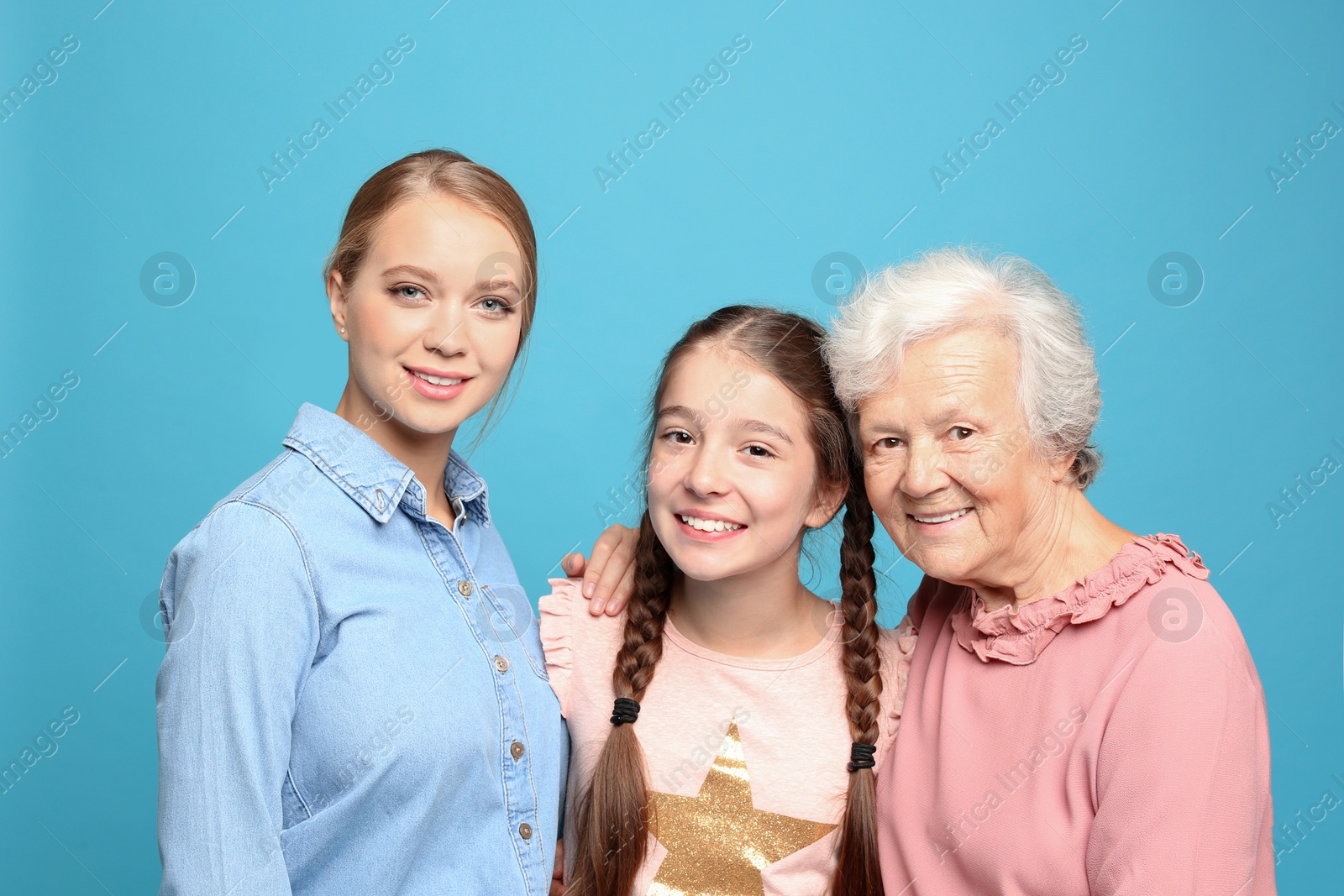 Photo of Happy sisters with their grandmother on light blue background