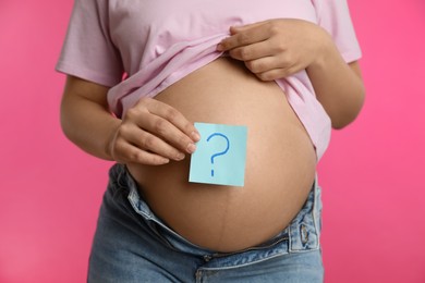 Photo of Pregnant woman with sticky note on belly against pink background, closeup. Choosing baby name