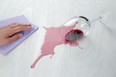 Photo of Woman cleaning spilled wine on white wooden table, closeup