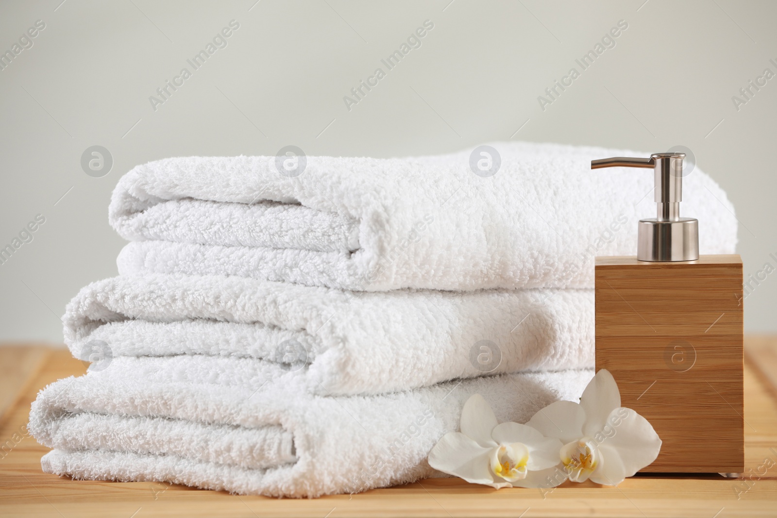 Photo of Stack of folded towels, orchid flowers and dispenser on wooden table