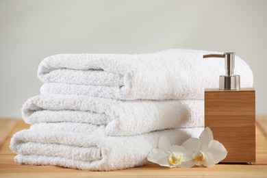 Photo of Stack of folded towels, orchid flowers and dispenser on wooden table