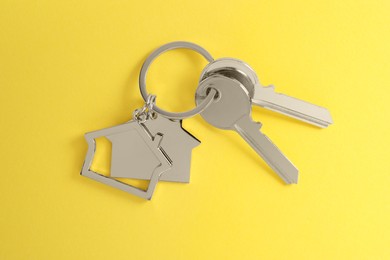 Photo of Keys with keychain in shape of house on yellow background, top view