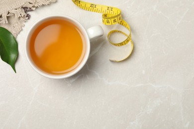 Photo of Flat lay composition with herbal diet tea and measuring tape on light marble table, space for text. Weight loss concept