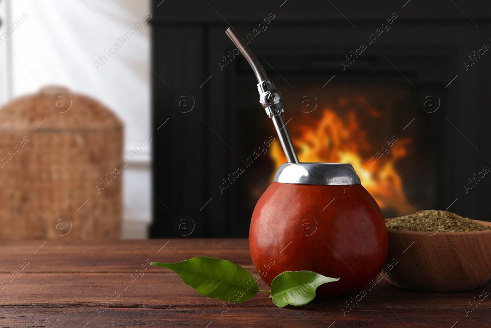 Image of Calabash with mate tea and bombilla on wooden table near fireplace. Space for text