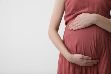 Photo of Young pregnant woman on light background, closeup. Space for text