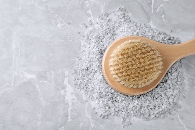 Photo of Salt for spa scrubbing procedure and brush on grey marble background, top view