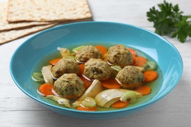 Photo of Bowl of Jewish matzoh balls soup on white wooden table