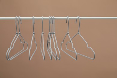 Photo of Empty clothes hangers on rack against light brown background