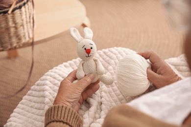 Elderly woman with knitted bunny at home, closeup. Creative hobby