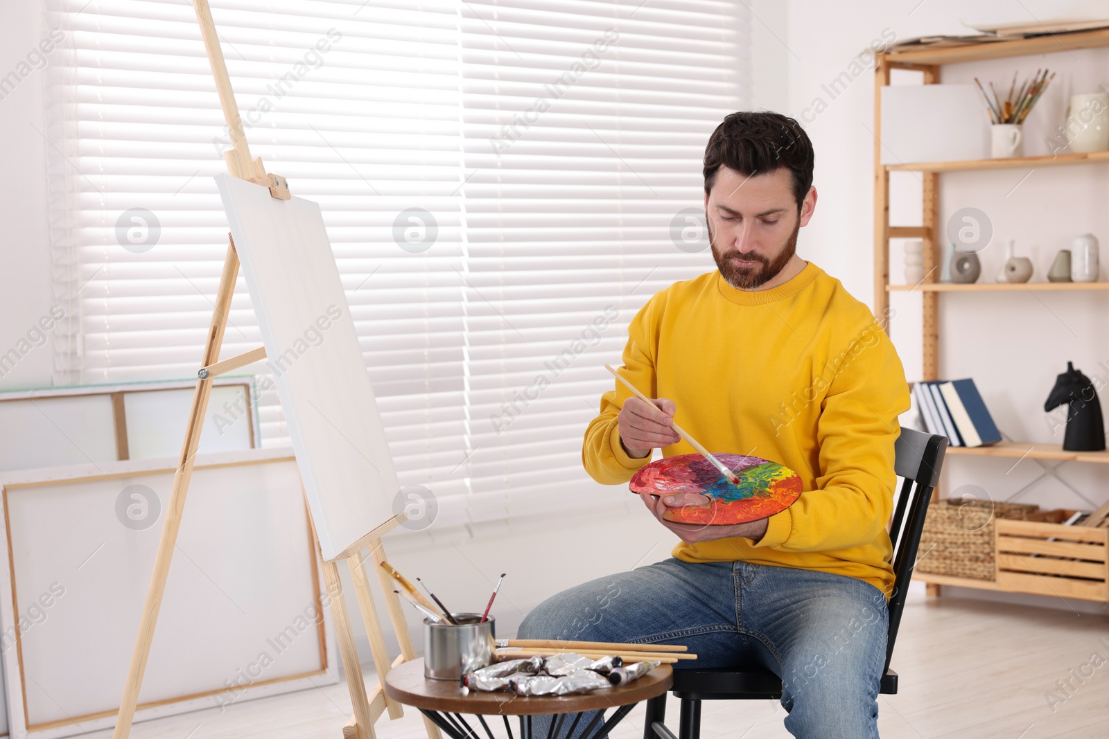 Photo of Man painting in studio. Using easel to hold canvas