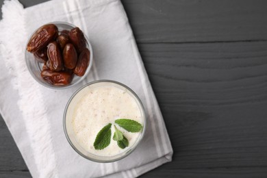 Glass of delicious date smoothie with mint and dried fruits on grey wooden table, flat lay. Space for text