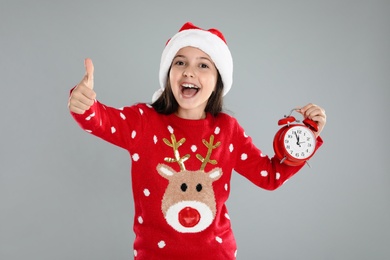 Girl in Santa hat with alarm clock on grey background. New Year countdown