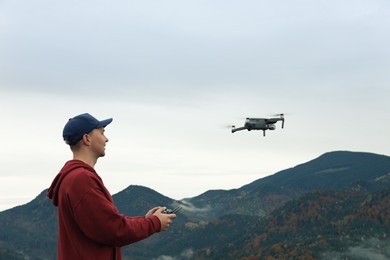 Young man operating modern drone with remote control in mountains