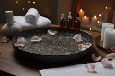 Bowl of water with flower petals on wooden table in spa