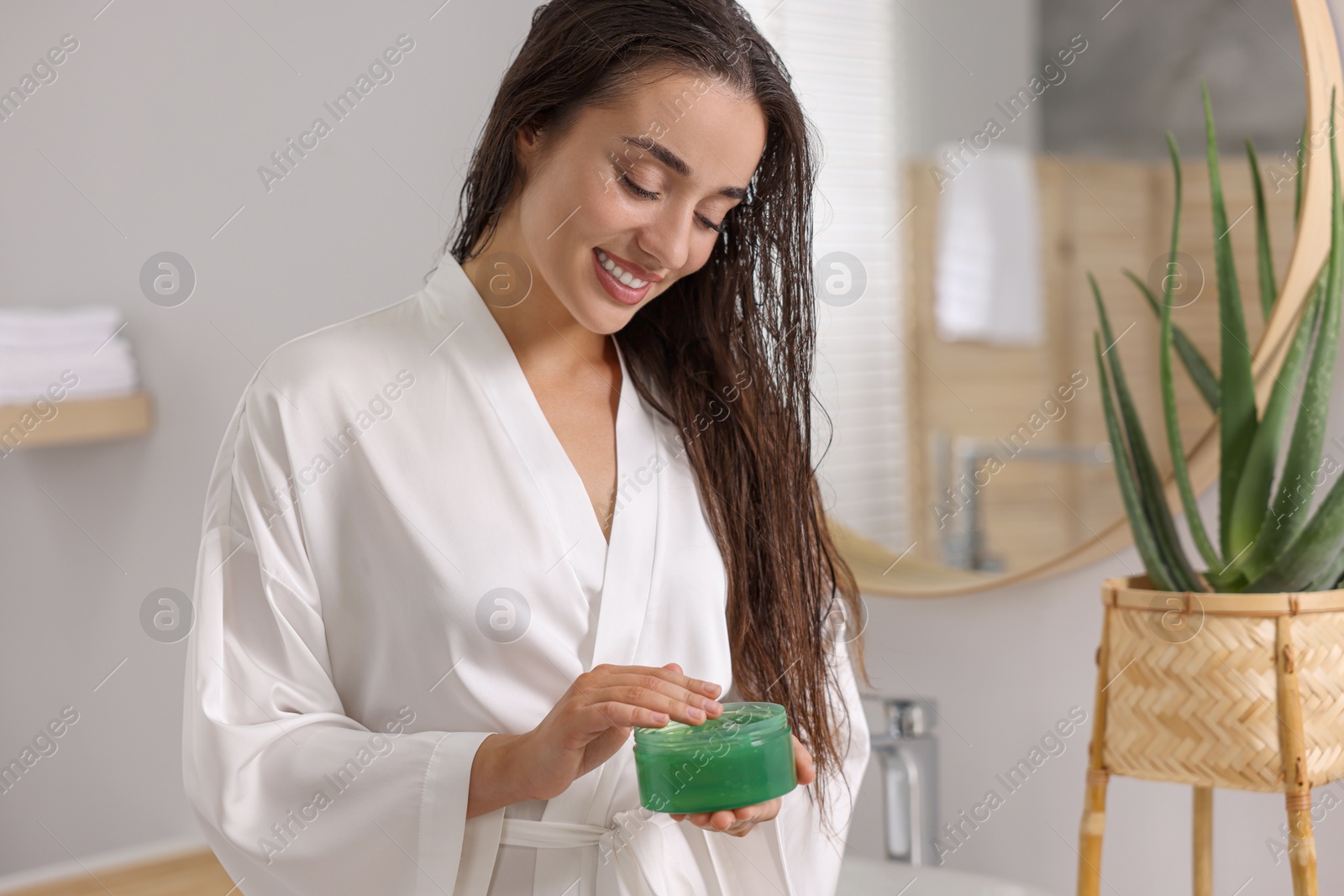Photo of Young woman holding jar of aloe hair mask in bathroom