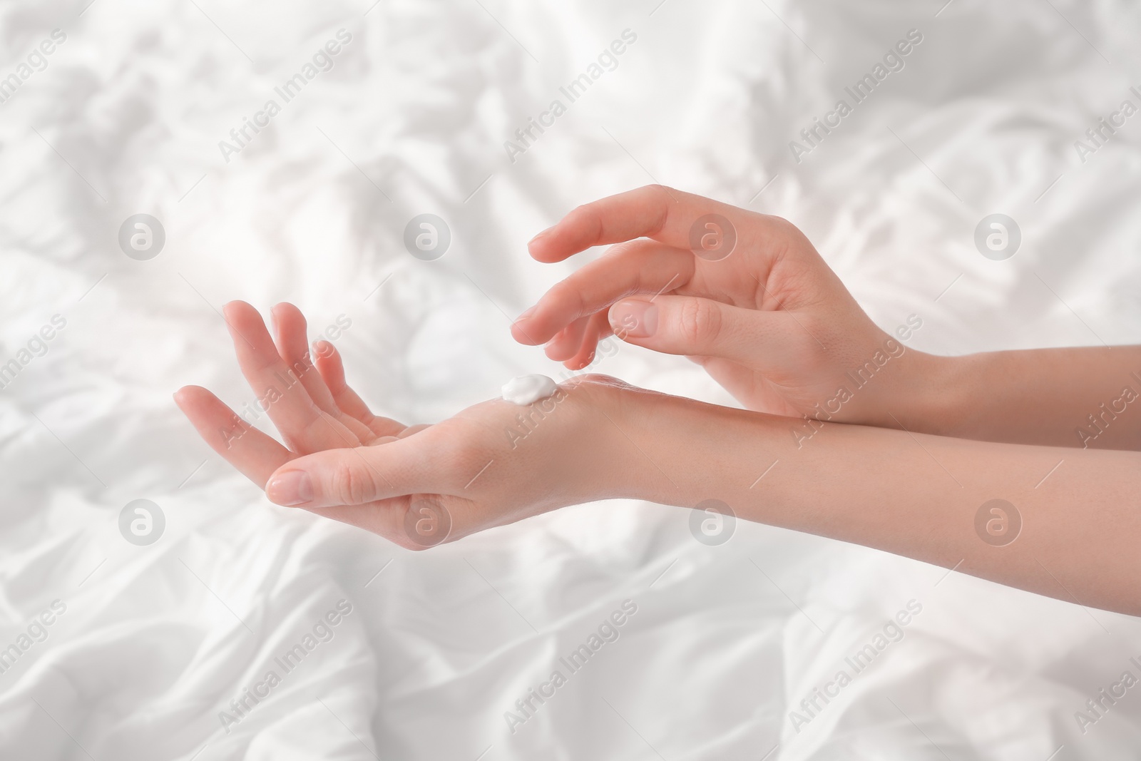 Photo of Young woman applying cream onto hands, indoors