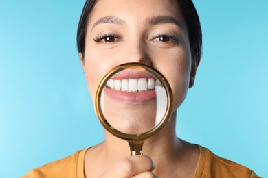 Photo of Young woman with healthy teeth and magnifier on color background, closeup