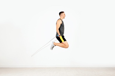 Young sportive man training with jump rope in light room