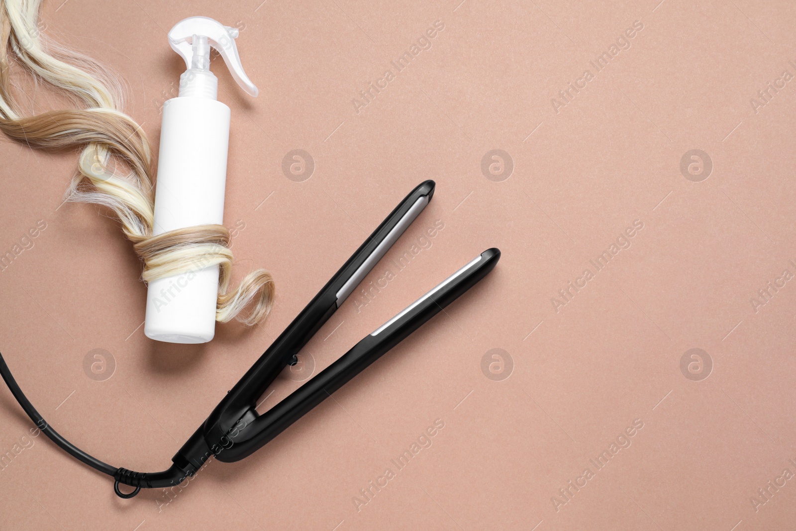 Photo of Spray bottle with thermal protection wrapped in lock of blonde hair and modern straightener on beige background, flat lay. Space for text