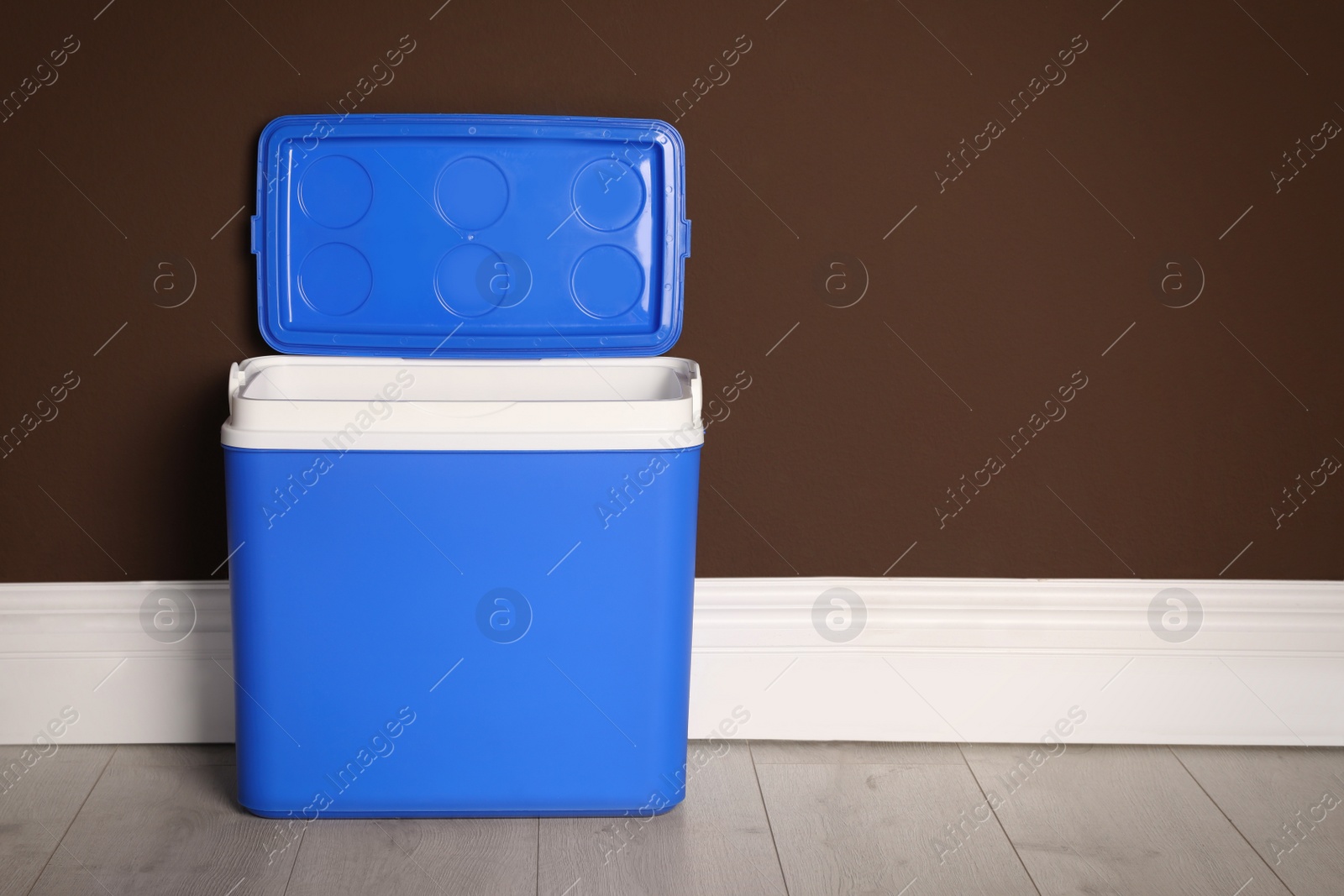 Photo of Open blue plastic cool box near brown wall. Space for text