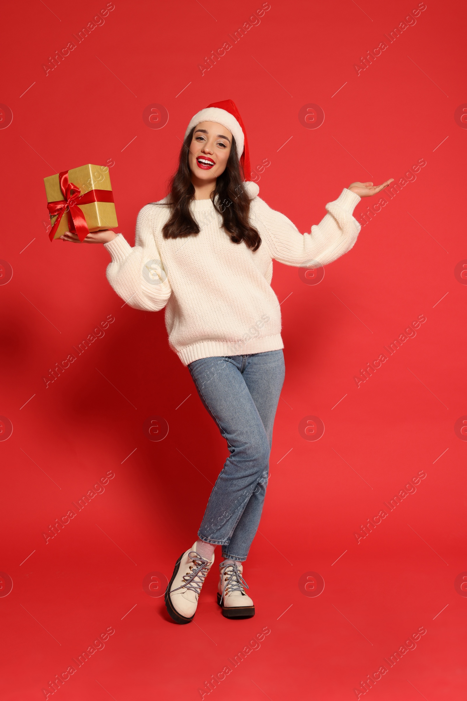 Photo of Beautiful young woman in Santa hat with Christmas gift on red background