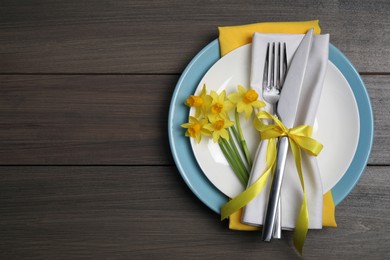 Photo of Festive table setting with narcissuses and cutlery on wooden table, top view with space for text. Easter celebration