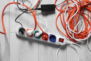 Photo of Power strip with different electrical plugs on white laminated floor, flat lay