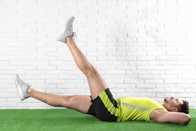 Handsome young man in sportswear doing scissors exercise on artificial green lawn near brick wall