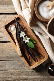 Photo of Vanilla pods, flowers, leaves and sugar on wooden table, top view