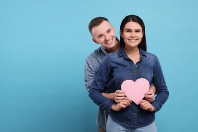 Lovely couple with decorative heart on light blue background, space for text. Valentine's day celebration