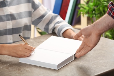 Photo of Writer signing autograph in book at table, closeup