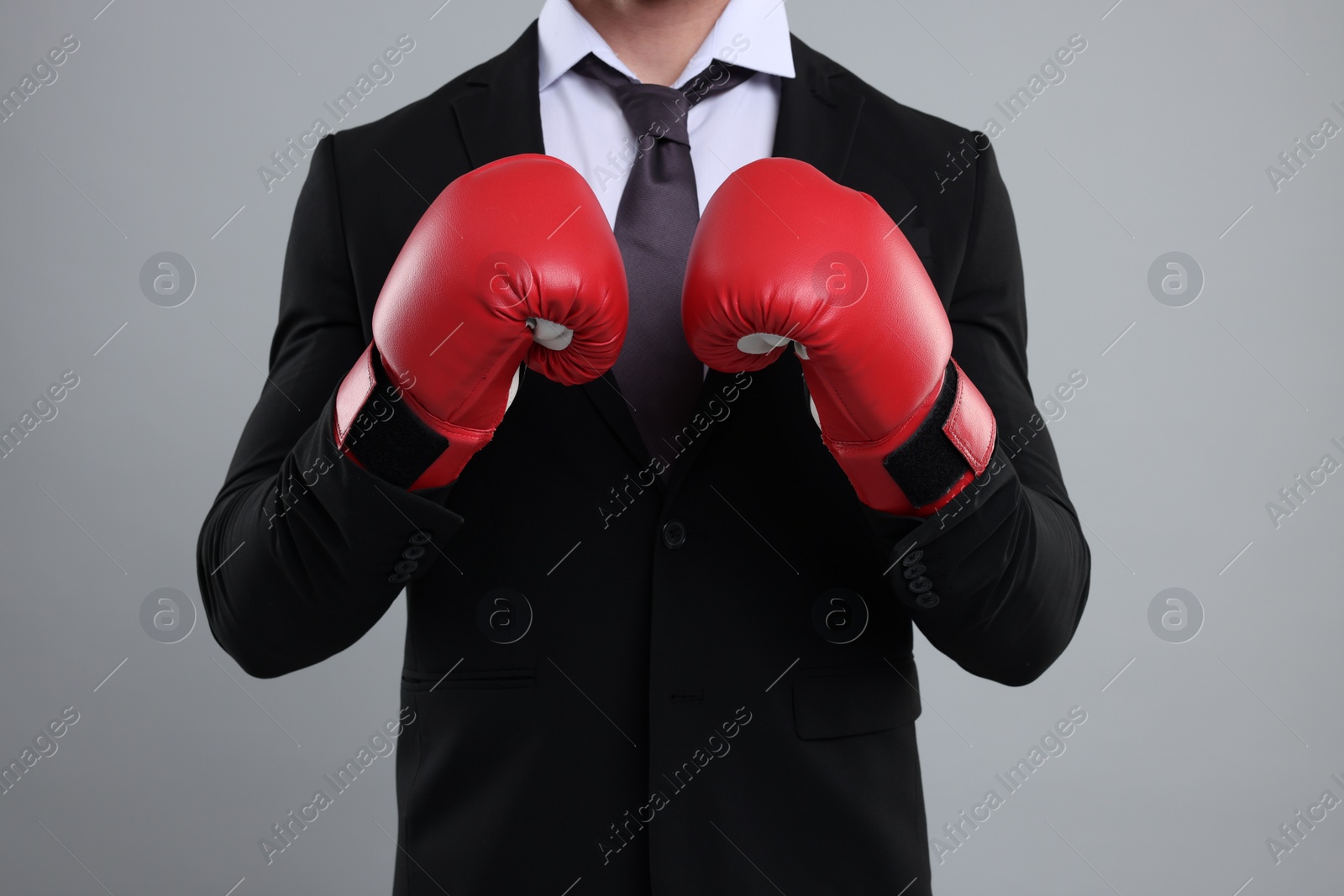 Photo of Businessman in suit wearing boxing gloves on grey background, closeup