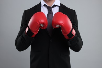 Businessman in suit wearing boxing gloves on grey background, closeup