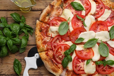 Photo of Delicious Caprese pizza with tomatoes, mozzarella and basil on wooden table, flat lay