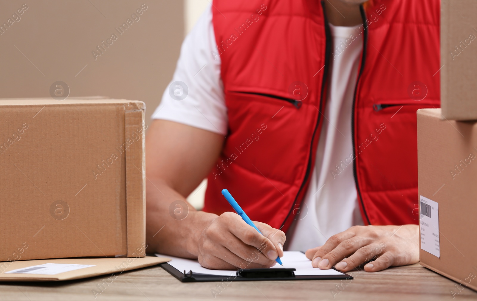 Photo of Young courier working with papers among parcels at table in delivery department