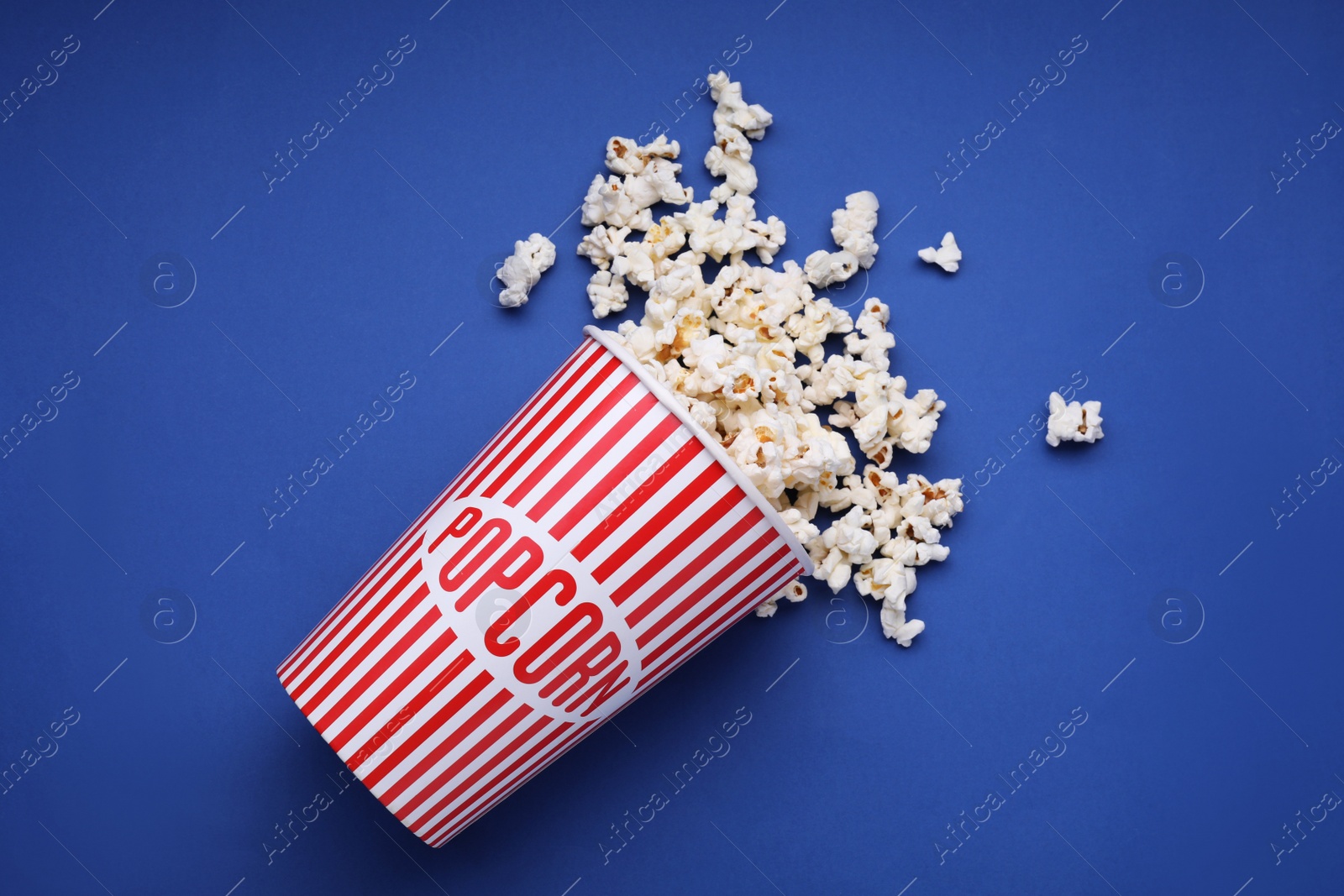 Photo of Bucket of tasty popcorn on blue background, flat lay