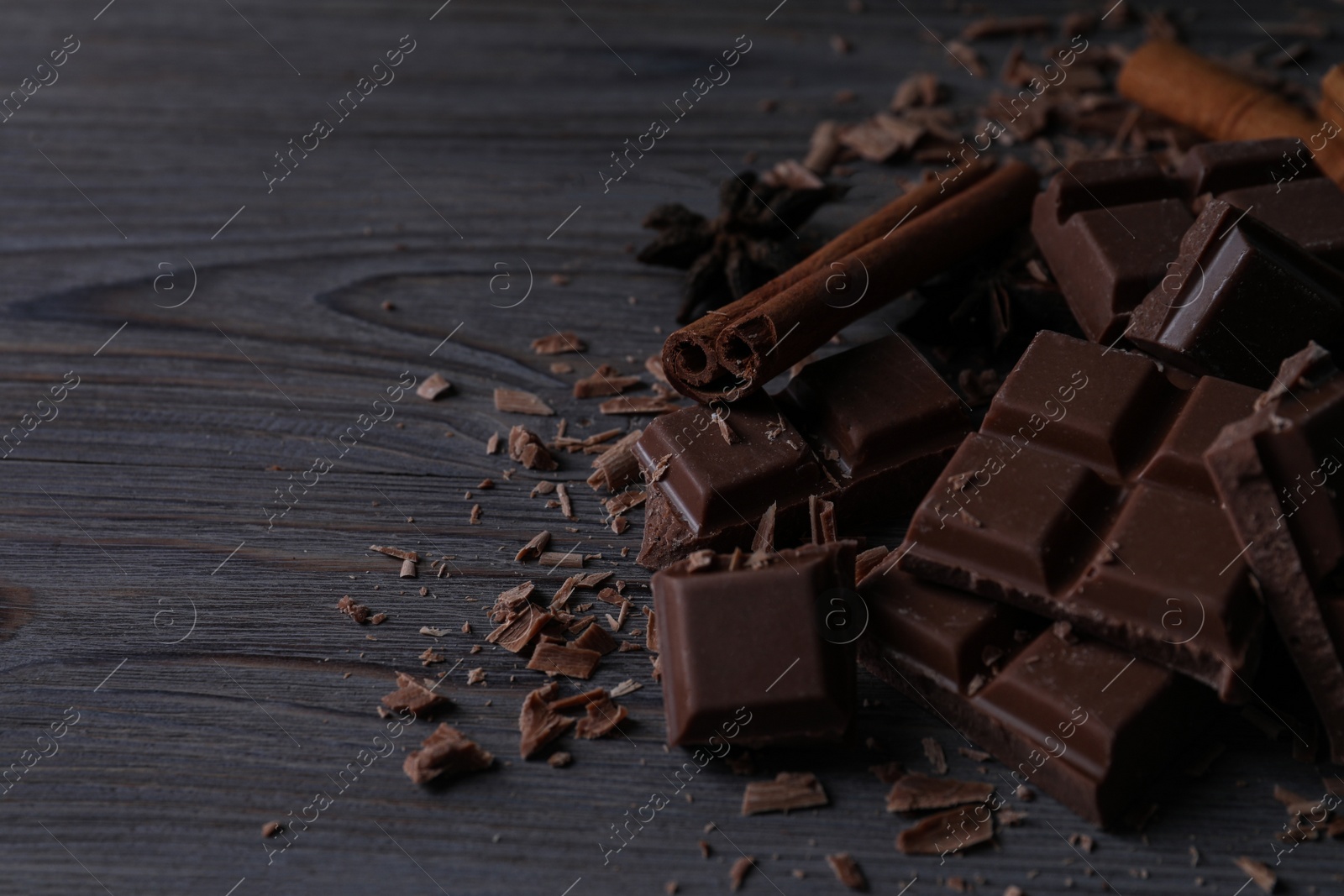 Photo of Delicious milk chocolate and cinnamon on wooden table. Space for text