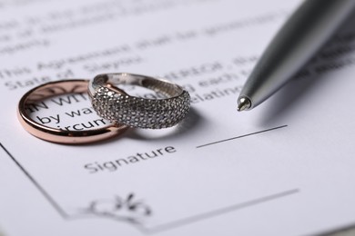 Photo of Marriage contract, pen and wedding rings, closeup