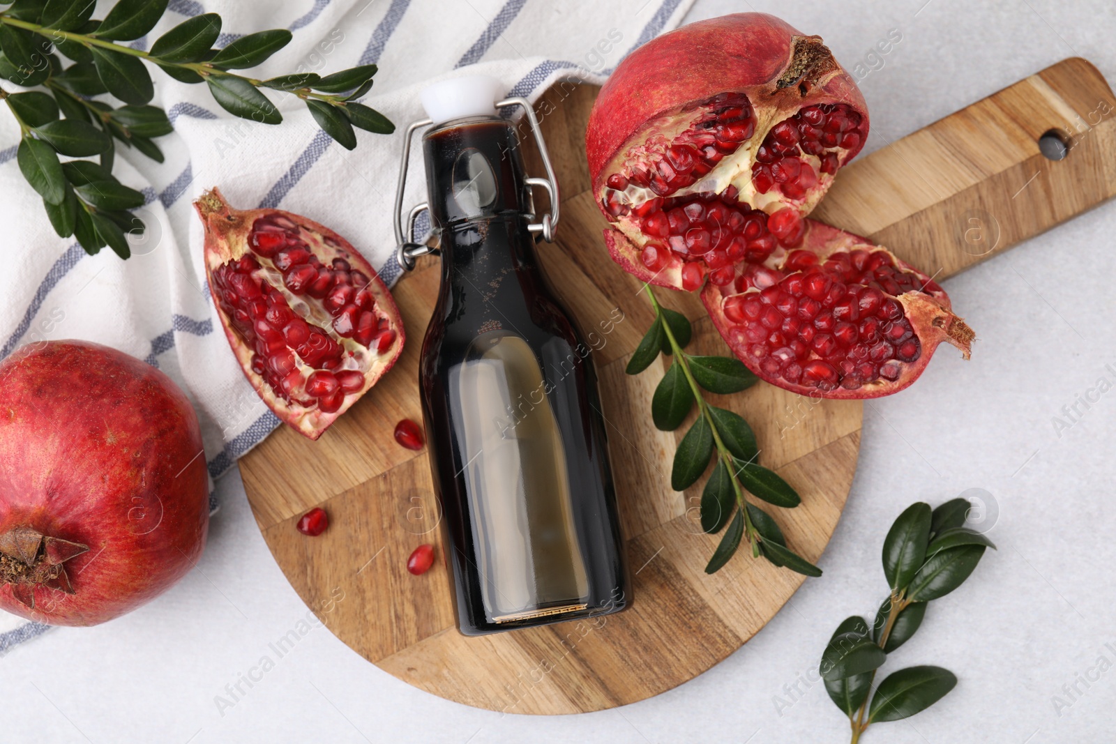 Photo of Tasty pomegranate sauce in bottle, branches and fruits on light table, flat lay