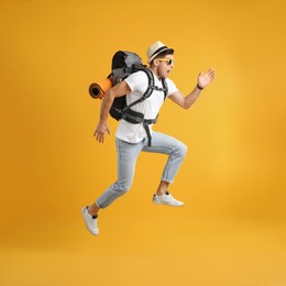 Photo of Emotional male tourist with travel backpack jumping on yellow background