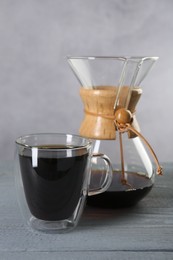 Photo of Glass and chemex coffeemaker with tasty drip coffee on grey wooden table