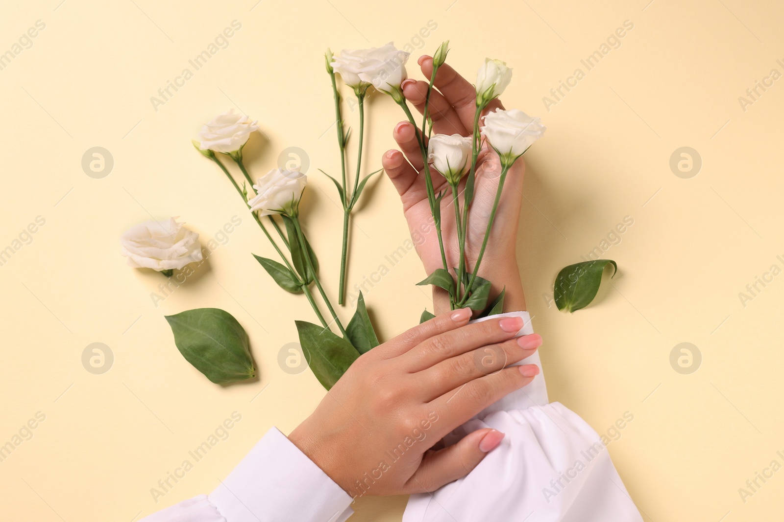 Photo of Woman with eustoma flowers on beige background, top view